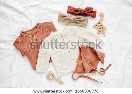 Set of  baby rompers, hat,  hairband and  knitted jumper on white bed. Fashion  baby clothes and accessories. Flat lay, top view