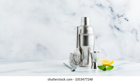 Set Of Bar Accessories For Cocktail Making. Shaker, Jigger, Strainer, Spoon On A Marble Background. Lemon And Mint Leaves. Copy Space