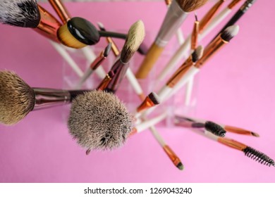 A set of beautiful different soft brushes for make-up from natural nap for beauty targeting and applying a tonal foundation in a stand and copy space on a pink, purple background.