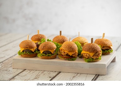 Surtido de pequeñas hamburguesas de carne y pollo con queso y lechuga con palos sobre un fondo de madera 