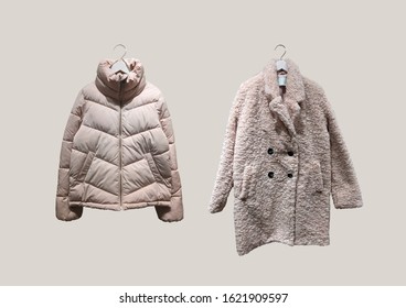 Set Of Beige Women Fashion Down Jacket And Fashionable Women Faux Shearling Coat On Hangers Isolated On Beige Background. Composition Of Clothes. Flat Lay, Top View, Copy Space. Winter Clothes Pattern