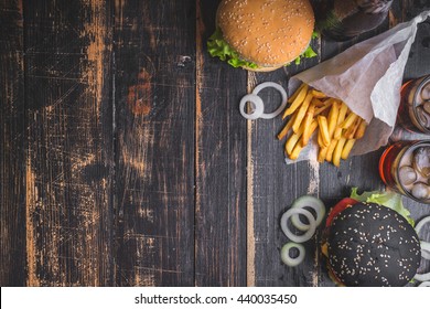 Set Of Black Burgers With Meat Patty, Cheese, Tomatoes, Mayonnaise, French Fries And Glass Of Cold Cola Soda With Ice From Above. Dark Wooden Rustic Background. Space For Text. Top View. Toned Image