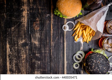 Set Of Black Burgers With Meat Patty, Cheese, Tomatoes, Mayonnaise, French Fries And Glass Of Cold Cola Soda With Ice From Above. Dark Wooden Rustic Background. Space For Text. Top View