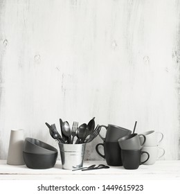 Set of black and grey crockery and cutlery against rustic white wooden wall. Simple kitchen utensils.