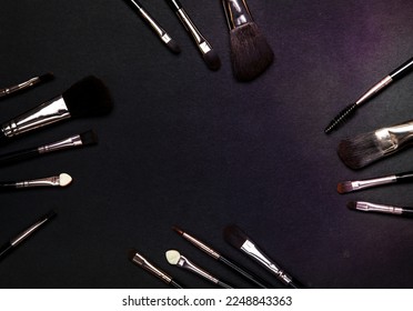 Set of black professional makeup brushes with black handles on black background. Top view, flat lay.
