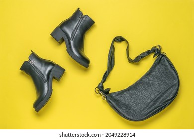 A set of black women's ankle boots and a leather bag on a yellow background. Fashionable leather things. Flat lay.