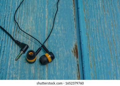 Set Of Black And Yellow Used Ear Buds On Blue Wood Grain Background.