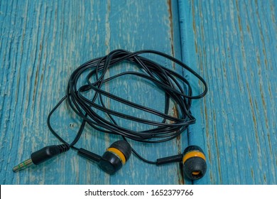 Set Of Black And Yellow Used Ear Buds On Blue Wood Grain Background.