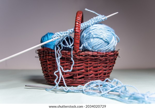 A set of blue wool thread\
balls of different sizes inside a wicker basket. Knitting needles\
and messy thread. At home hobby. Crocheting. Balls of\
yarn.