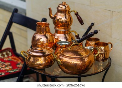 A Set Of Bright Copper Dishes Stands On A Round Glass Table Next To The Chair