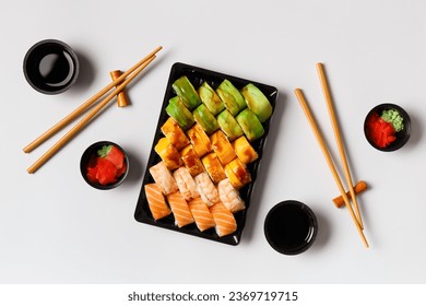 A set of bright multi-colored sushi rolls with shrimp, salmon, avocado in plastic packaging, Chinese chopsticks, sauce, ginger on a white background, top view. Sushi delivery - Powered by Shutterstock