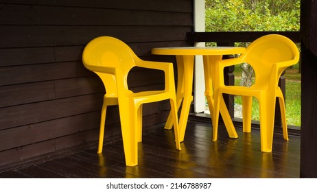 A Set Of A Bright Yellow Plastic Table And Two Chairs Sits On A Dark Wood Outdoor Terrace In A Nature House. High Quality Photo