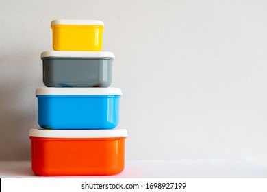 A Set Of Brightly Coloured (yellow, Grey, Blue, Orange) Plastic Containers Stacked By Height Against An Off-white Background