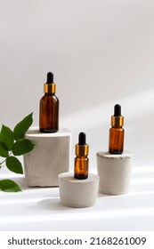 Set of brown glass dropper bottles with a pipette on concrete podiums, green leaves. Organic, natural cosmetics. Beauty, skin care. Spa products. Close up, copy space. Selective focus