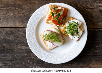 Set of Bruschett with cream cheese and tomato spread. Radish, micro green and flaxseed in food. Simple food on the plate. Healthy breakfast in a white plate top view. Wooden background. Cracker.