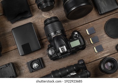 A set of camera and photographic equipment (lens, tripod, filter, memory card, hard disk) on a wood table. Professional photographer accessories background.