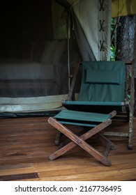 Set of camping wooden chair with green fabric seat and footrest on the terrace in front of the room of large tent. Folding outdoor sunbed on white glamping tent, vertical style.