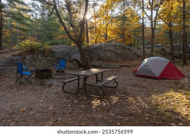 Set up campsite with a tent, camping chars, picnic table, and firepit in the fall forest. Early morning, sun low over horizon. Killbear Provincial Park, Ontario, Canada. - Powered by Shutterstock