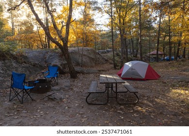 Set up campsite with a tent, camping chars, picnic table, and firepit in the fall forest. Early morning, sun low over horizon. Killbear Provincial Park, Ontario, Canada. - Powered by Shutterstock