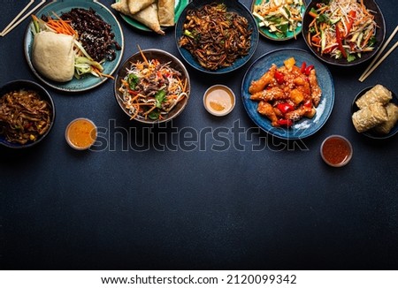 Set of Chinese dishes on table: sweet and sour chicken, fried spring rolls, noodles, rice, steamed buns with bbq glazed pork, Asian style banquet or buffet, top view with copy space
