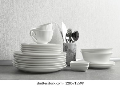 Set of clean dishes and cutlery on table near light wall
