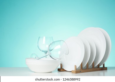 Set of clean dishes and glasses on table against color background