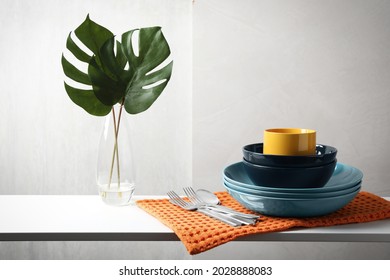 Set of clean dishware, cutlery and tropical leaves on white table