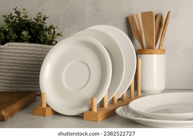 Set of clean plates and different kitchen utensils on light table near wall