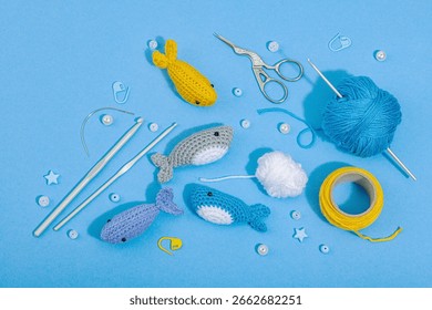 Set of clew of thread for knitting. Crocheted different fishes, handmade, sea hobby concept. Props and special craft tools on blue background, top view