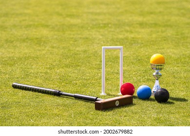 a set of colored balls, a hammer and a winners prize at the croquet hoop on the green lawn