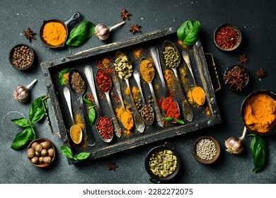A set of colored spices in a wooden box. On a black slate background. Top view.
