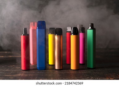 Juego de cigarrillos electrónicos desechables coloridos sobre un fondo de madera oscura con humo. El concepto de tabaco moderno, vaporización y nicotina.