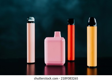 A set of colorful disposable electronic cigarettes of different shapes on a black background with smoke. Concept of modern smoking, vaping and nicotine.