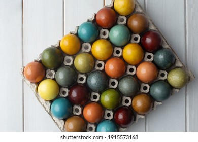 Set of colorful easter eggs colored with natural dye - turmeric, onion skin, carcade, red cabbage and coffee in cardboard on white wooden background.