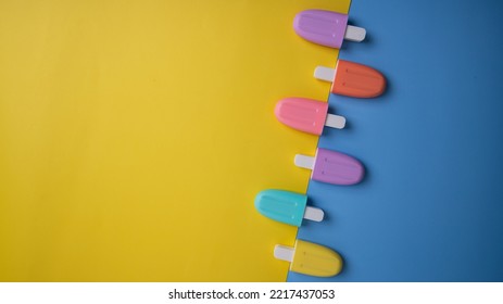 A Set Of Colorful Ice Pops, Isolated On Yellow And Blue Background. A Selective Focus Photo Of The Ice Pop. A Dessert Concept Photo.