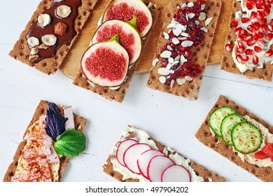 Set Of Crisp Rye Bread Sandwiches With Ham, Radish, Cucumber, Fig, Cranberry Jam, Soft Cheese And Chocolate Paste Over White Background. Top View.