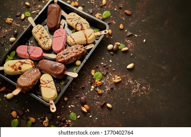 Set of delicious white and milk chocolate and strawberry ice cream on a stick served in metal tray. Placed on rusty background. Flat lay, top view with copy space