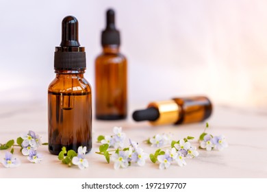 Set Of Different Bottles With Beauty Serum, Hyaluronic Acid And Vitamins On Light Background With Wild Flowers. Home Spa Concept.