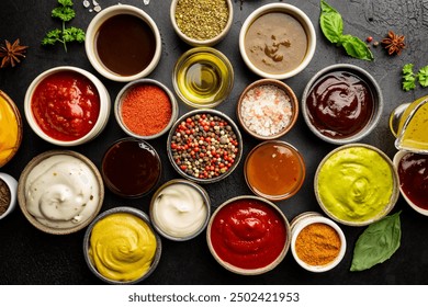 Set of different bowls of various dip sauces, on dark background, top view