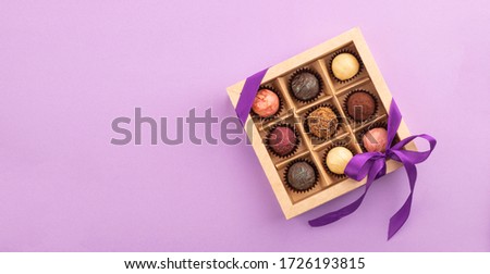 Set of different chocolates in a paper box with a satin purple ribbon on a bright background. Holiday concept.