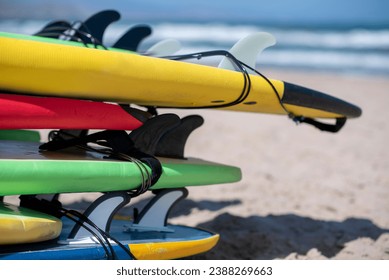 Set of different color surf boards in a stack by ocean. Surf boards for rent on sandy beach. Soft toned photo. - Powered by Shutterstock