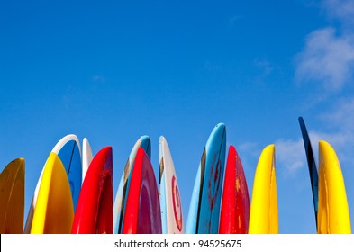 Set of different color surf boards in a stack by ocean