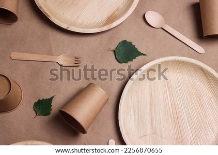 Set of different eco-friendly tableware with green birch leaves on brown paper  background. Bamboo plates, paper cups and wooden cutlery. Zero waste, plastic free, disposable tableware. Top view.