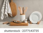 Set of different kitchen utensils and plates on white near gray wall