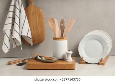 Set of different kitchen utensils and plates on white near gray wall