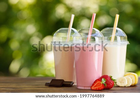 set of different milkshakes in disposable plastic glasses on wooden table outdoors