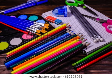 Set of different school stationeries. Notepad, scissors, pensils, paints, paintbrushes on rustic wooden desk. Back to school