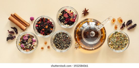 A set of different types of green, black and herbal tea next to the kettle filled with hot brewed tea on a beige background. Delicious organic drinks. View from above. Banner - Shutterstock ID 1922584361