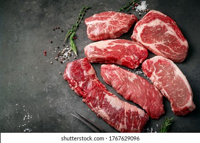 A set of different types of raw beef steaks: rib eye, Striploin, Denver, machete, top blade on a dark stone background. - Shutterstock ID 1767629096