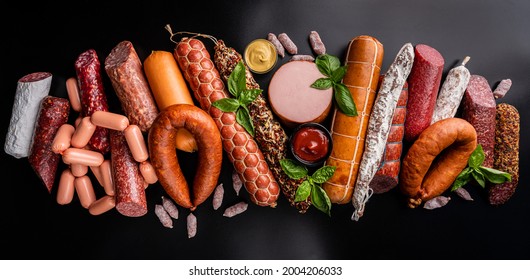 Set of different types of sausages, salami and smoked meat with basil and spices on a black background. Top view. banner - Shutterstock ID 2004206033